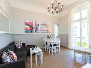 A modern living room with a sofa, a dining table, and a chandelier.