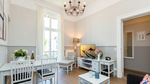 Un salon moderne comprenant un coin repas, un lustre, un téléviseur et une vue sur l’extérieur.