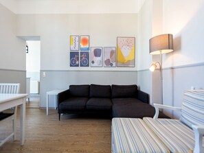 Ein modernes Wohnzimmer mit einem dunklen Sofa, gestreiften Sesseln und einer Stehlampe. An der Wand befinden sich abstrakte Gemälde und ein weißer Tisch steht in der Ecke.