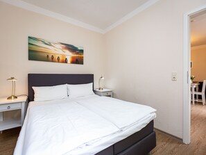 Cama bem arrumada com lençóis brancos, cabeceira escura e duas mesas de cabeceira com luminárias.