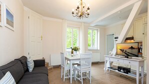 A modern living room with a grey sofa, white dining table, and chairs, a chandelier, and a television on a white cabinet. - Villa Amelia, apt. 09 (Heringsdorf)