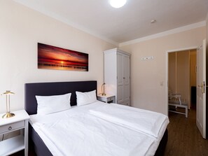 Et pænt møbleret soveværelse med en stor seng, et natbord, en lampe, et skab og et billede på væggen.