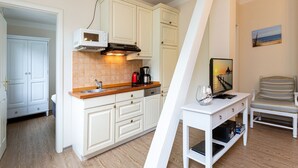 A compact kitchen with white cabinetry, a wooden countertop, and a dining area with a striped chair. - Villa Amelia, apt. 09 (Heringsdorf)