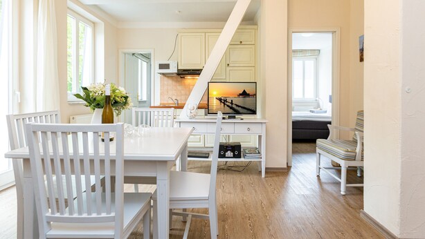 A bright, spacious kitchen with white cabinetry, a dining area with white chairs, and a view of the sea through a window. - Villa Amelia, apt. 09 (Heringsdorf)