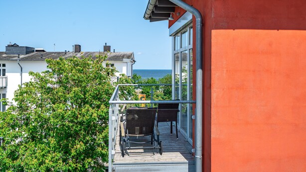 Un balcon avec vue sur la mer, un immeuble rouge et un arbre.