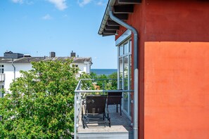 Un balcon avec vue sur la mer, un immeuble rouge et un arbre.