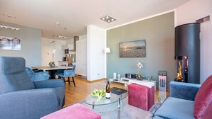 Un salon moderne avec une table basse en verre, une cheminée et un coin repas avec des chaises bleues.