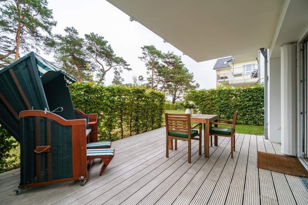 An outdoor deck with a wooden table and chairs, a wicker sofa, and a view of a residential building and trees.
