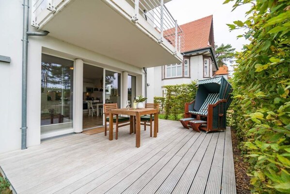 Eine Holzterrasse mit Tisch und Stühlen, ein grüner Outdoor-Stuhl und eine Glastür, die zu einem Raum führt.
