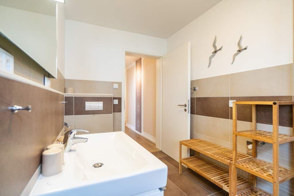 A modern bathroom with a large sink, a mirror, a wooden shelf, and a towel rack.