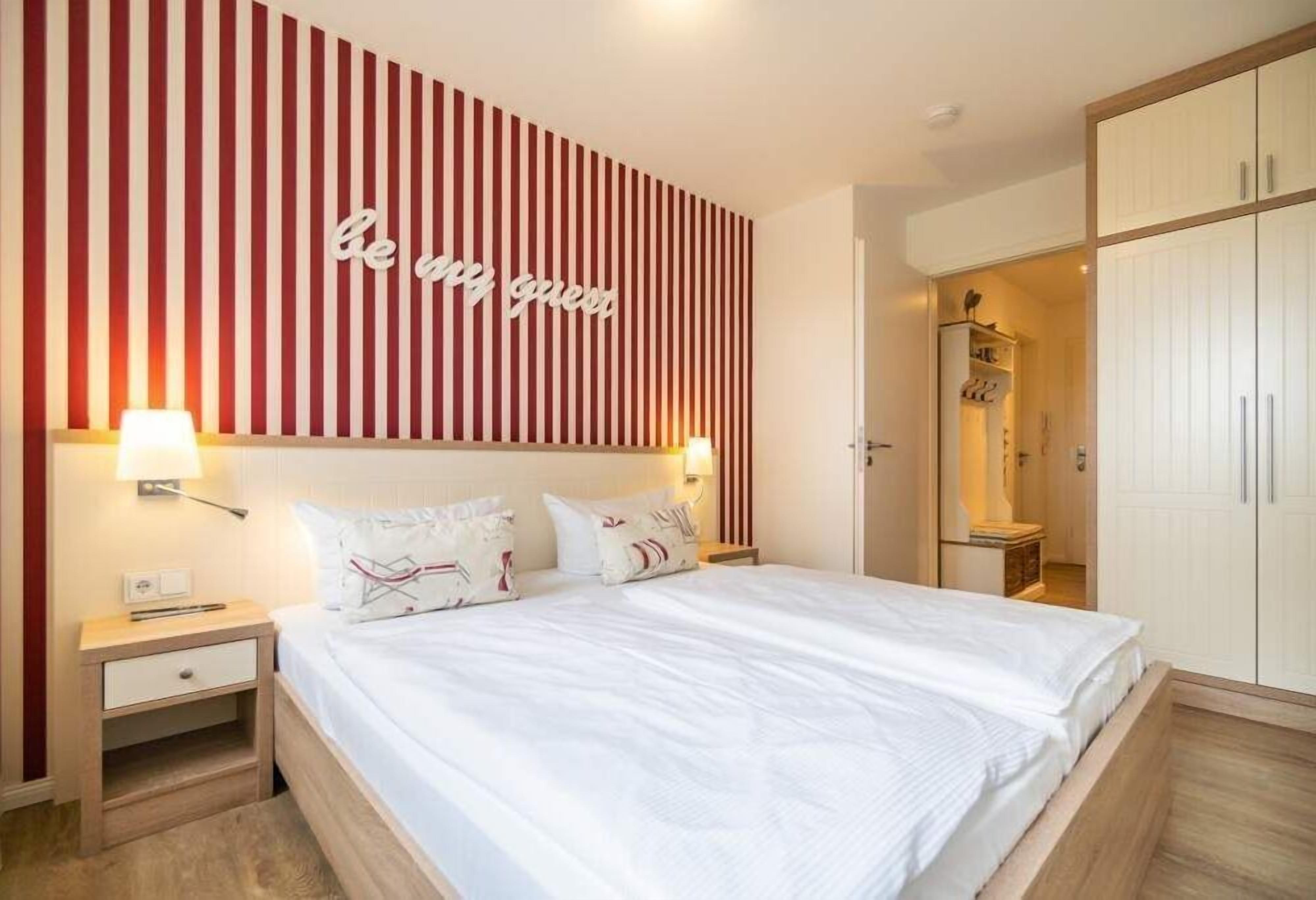 A hotel room with a bed, bedside tables, a wardrobe, and a striped wall with a motivational quote.