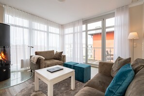 Uma sala de estar moderna com lareira, um conjunto de sofás, uma mesa de centro e uma vista através de amplas janelas.