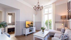 Moderni olohuone, jossa on litteänäyttöinen televisio, valkoinen sohvapöytä, sohva ja kattokruunu.
