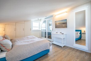Ein Schlafzimmer mit Bett, Kommode, Spiegel und Fenster.