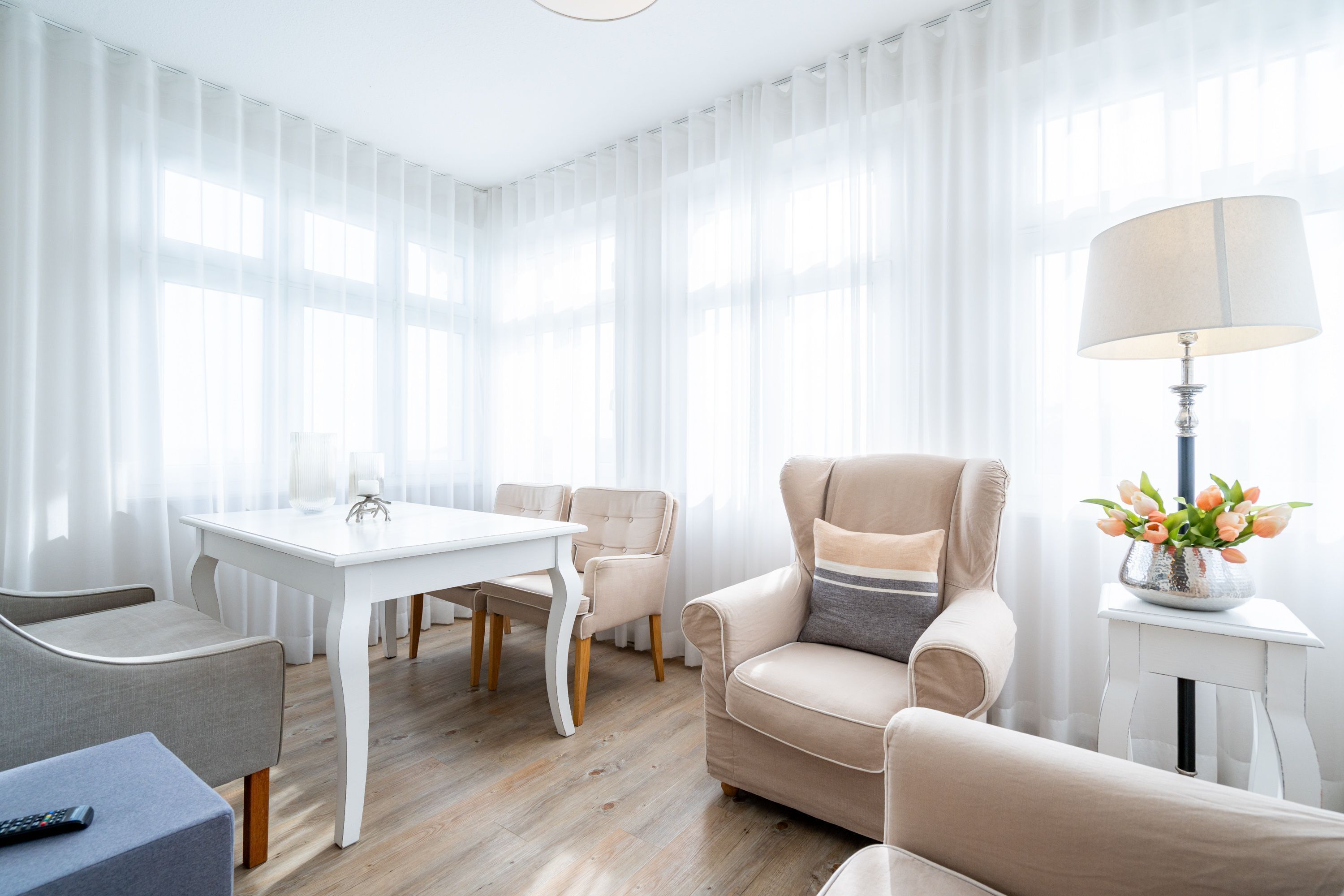 Una sala moderna con una mesa de comedor blanca, sofás color beige y una lámpara en una mesita auxiliar.