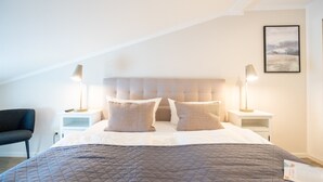 Quarto com uma cama grande, duas mesas de cabeceira, uma cadeira e um quadro pendurado na parede.