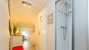 Ein modernes Badezimmer mit Duschkabine aus Glas, einem kleinen Hocker und einem an der Wand befestigten Ablagebereich mit Dekoration.