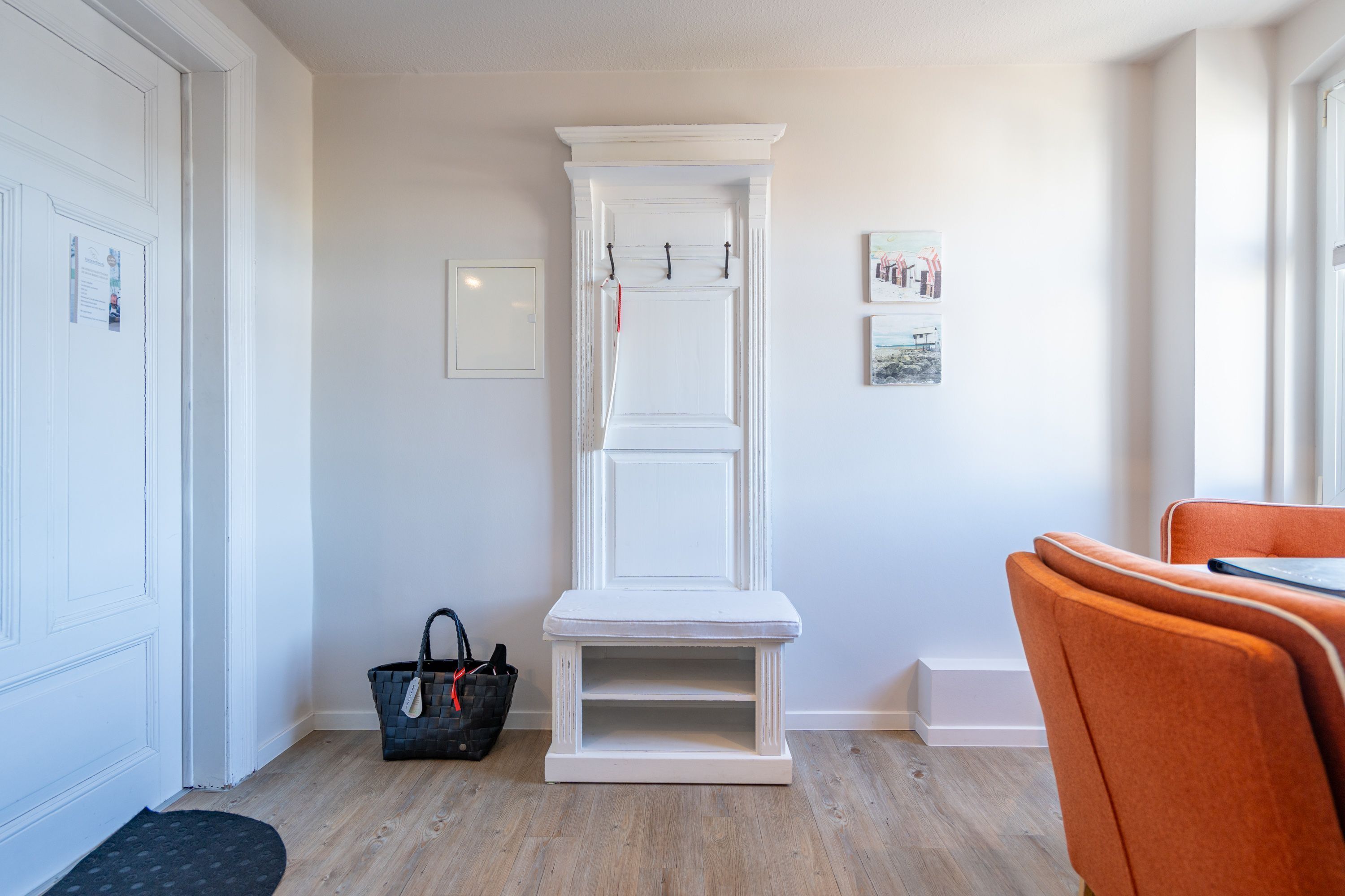 A hallway with a white bench, a basket, and a door with a mat.