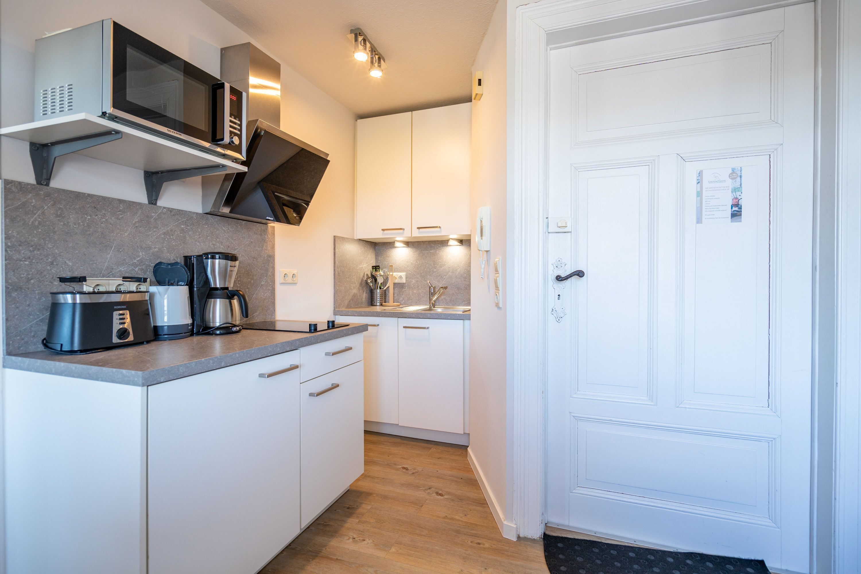 Una cucina moderna con mobili bianchi, un forno a microonde, una moka e un tostapane.