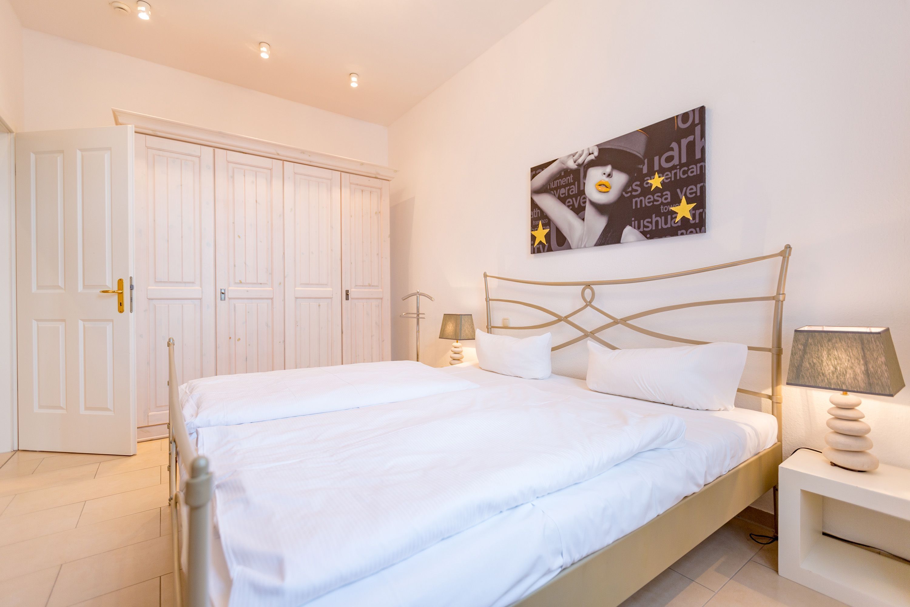 Una camera da letto con un letto grande, pareti bianche, una porta e un'opera d'arte a parete.