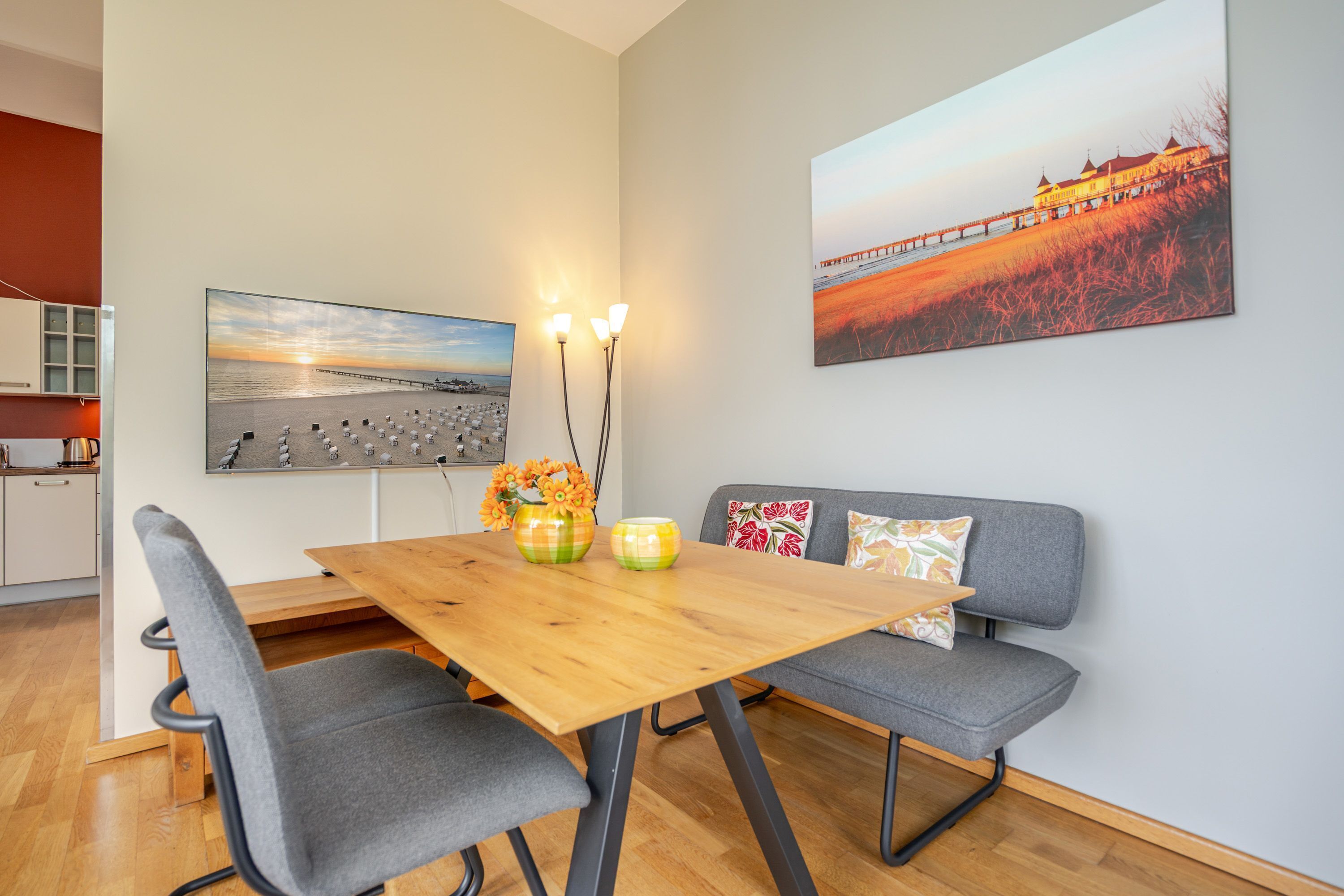 A dining area with a wooden table, grey upholstered chairs, and a sofa with patterned cushions.