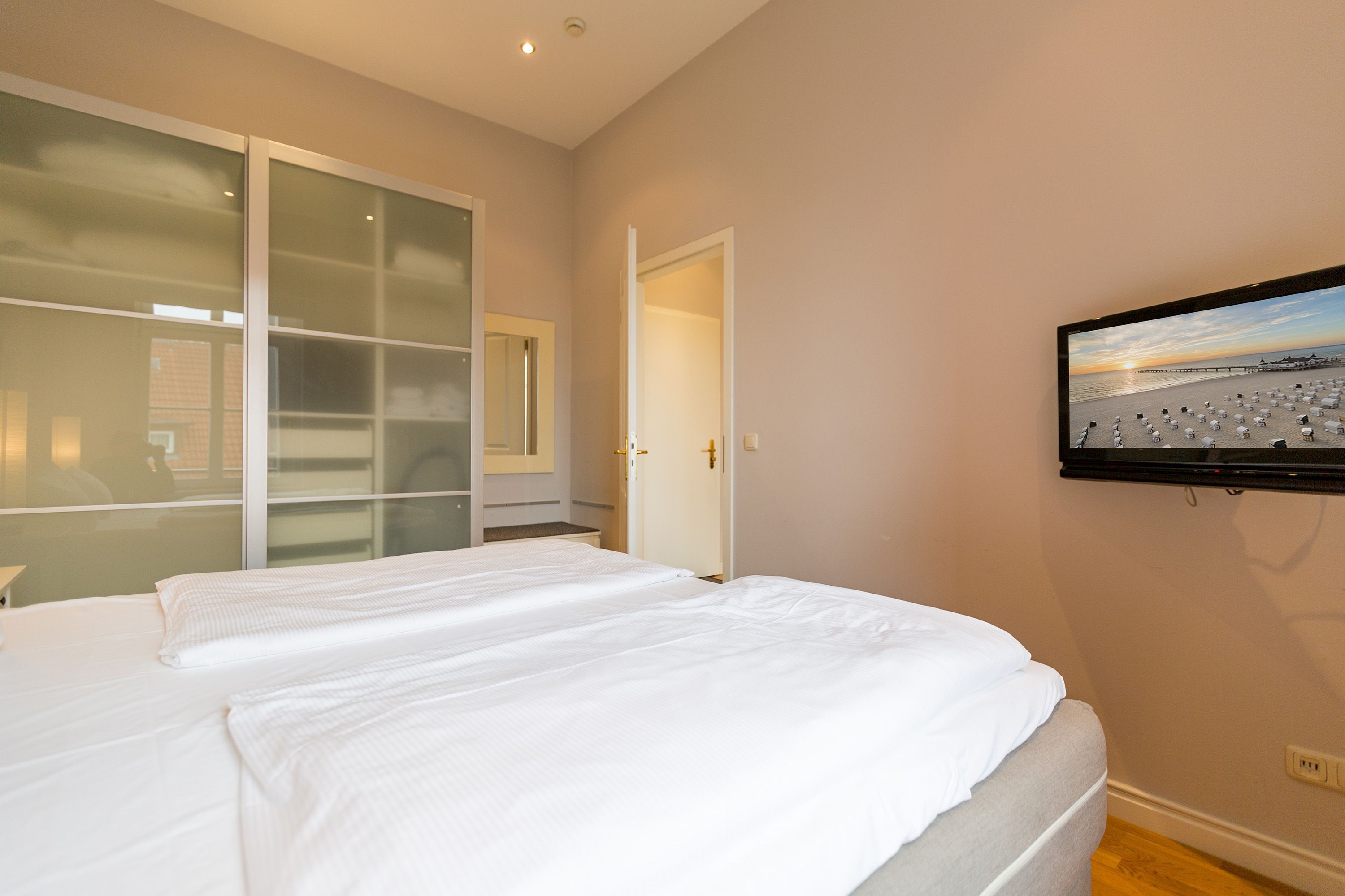 Ein Schlafzimmer mit zwei Betten, einem Schiebeglastüren-Kleiderschrank und einem an der Wand montierten Fernseher.
