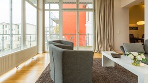 Un soggiorno moderno con una grande finestra, un divano bianco, un tavolino da caffè e vista su un edificio rosso.