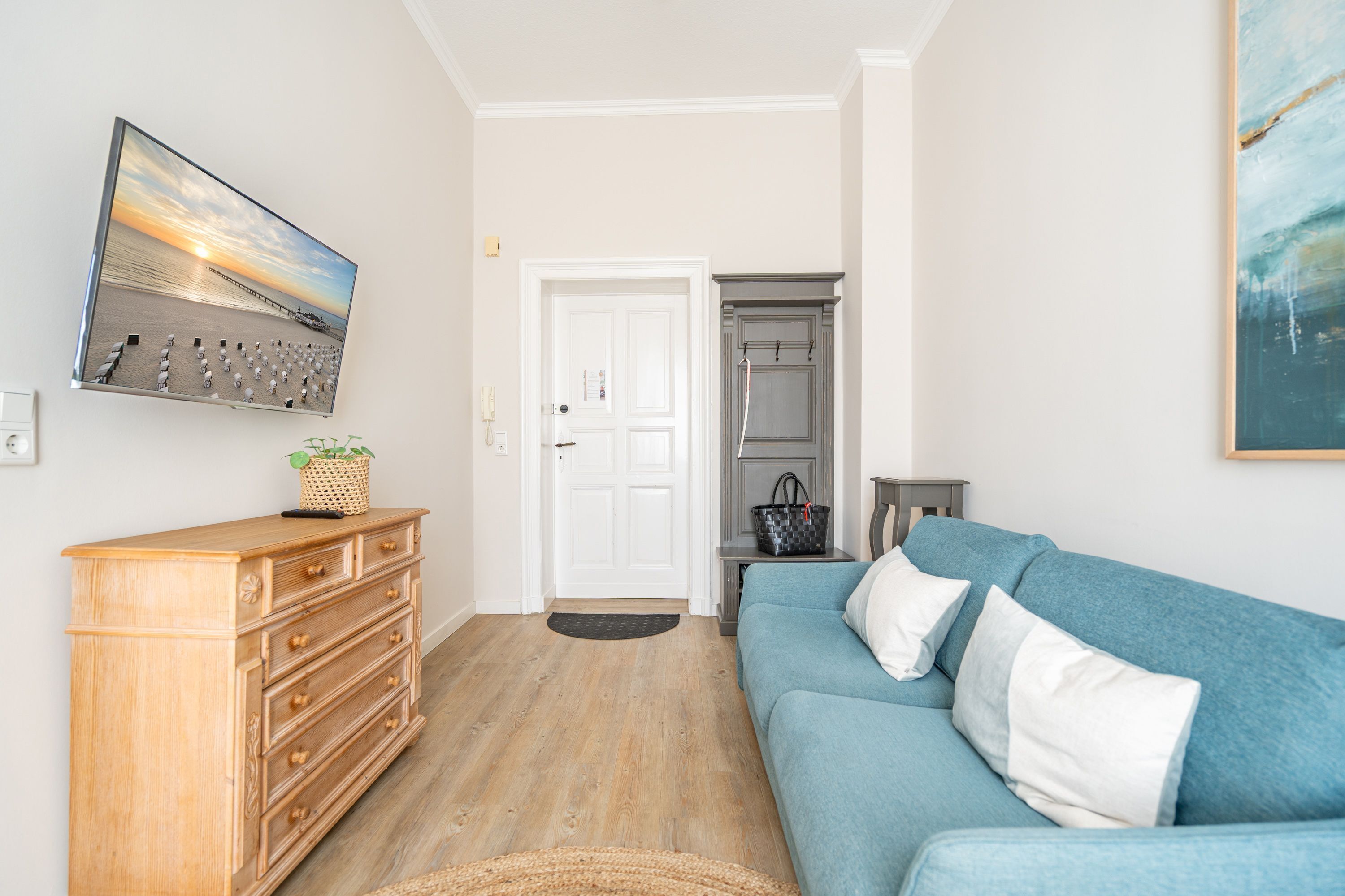 Een woonkamer met een houten dressoir, een blauwe bank en een flatscreen televisie aan de muur.