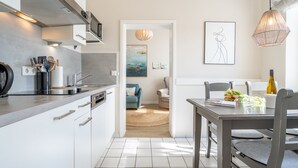 A modern kitchen with white cabinets, a built-in oven, and a dining area with a table and chairs. - Villa Albertine, App. 07 (Heringsdorf)