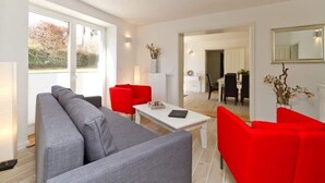 A modern living room with a grey sofa, red chairs, a white coffee table, and a dining area in the background. - Villa Arcadia, App. 10 (Heringsdorf)