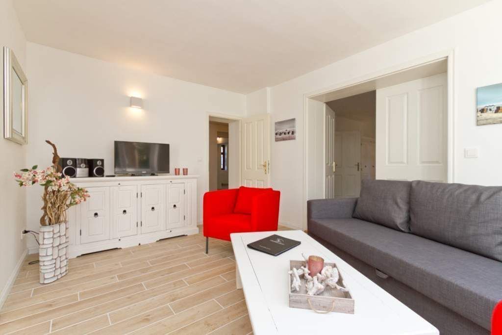 Una sala de estar moderna con un aparador blanco, sofás rojos y grises, una mesa de centro blanca y un televisor.