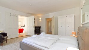 A hotel room with a large bed, a chair, a desk, and a red chair in the background. - Villa Arcadia, App. 10 (Heringsdorf)