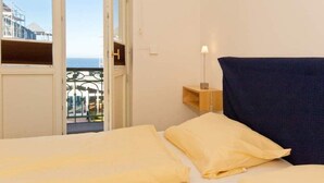 Een hotelkamer met een bed, een nachtkastje, een lamp en uitzicht op de zee door een balkondeur.