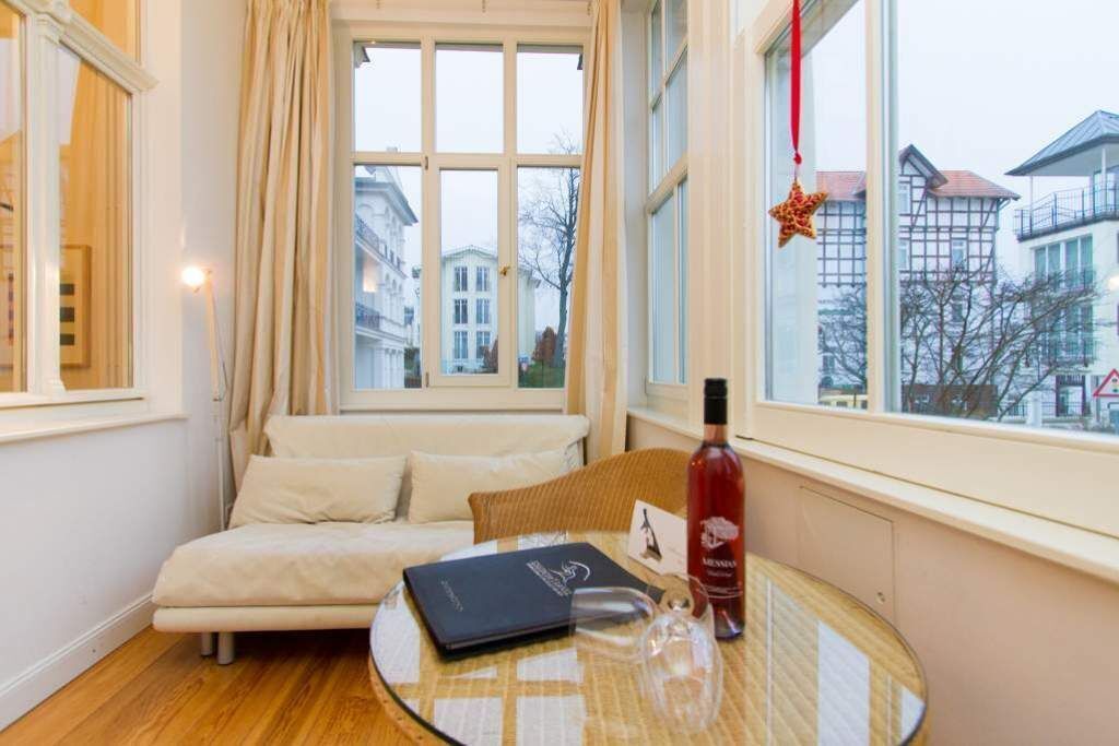 A cozy room with a sofa, a table with a bottle and glasses, and a window with a view of buildings.
