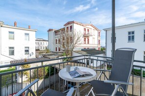 Een balkon met een tafel, stoelen en uitzicht op omliggende gebouwen.