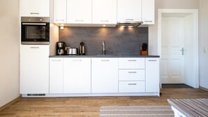 Una cocina moderna con armarios blancos, horno integrado, cafetera y pileta de acero inoxidable.