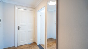 Un pasillo con una puerta blanca, suelo de madera y un espejo grande en la pared.