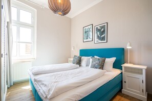 A bedroom with a bed, white nightstands, a blue headboard, and two framed pictures on the wall.