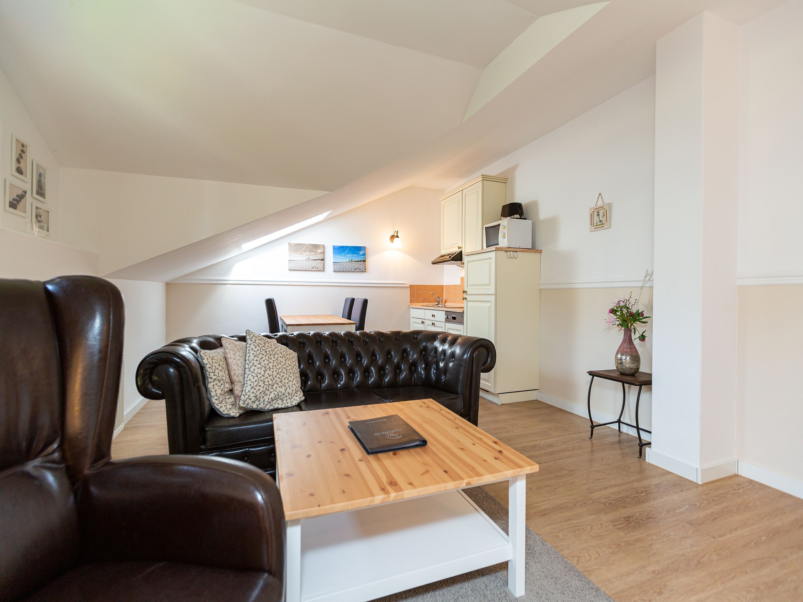 A cozy living room with a leather sofa, a wooden coffee table, and a dining area with a table and chairs.