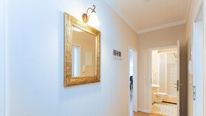 A hallway with a large ornate mirror, a light fixture, and a door leading to a bathroom. - Villa Arcadia, apt. 07 (Heringsdorf)