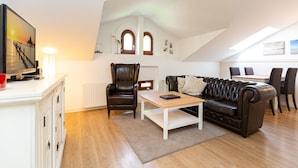 A modern living room with a leather sofa, a wooden coffee table, a TV on a white cabinet, and a dining area with chairs and a table. - Villa Arcadia, apt. 07 (Heringsdorf)