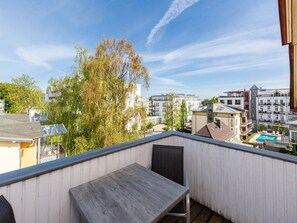 Un balcón con mesa y sillas, con vista a una piscina y edificios.
