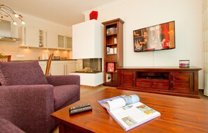 Una sala de estar con un sofá morado, una mesa de centro con un control remoto y una revista, un mueble de entretenimiento de madera y un televisor de pantalla plana montado en la pared.
