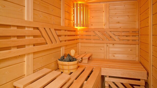 Puisesta laudeseinästä ja kivistä koostuva sauna, jossa on myös ämpäri.