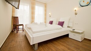 Moderni hotellihuone, jossa on suuri sänky, tuoli, yöpöytä ja seinälle asennettu televisio.