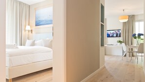A hotel room with a bed, a desk, a TV, and a view of the sea. - Dünenpalais, App. 01 (Heringsdorf)