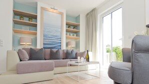 A modern living room with a sofa, a coffee table, and a chair. There are shelves with plants and a painting on the wall. - Dünenpalais, App. 01 (Heringsdorf)