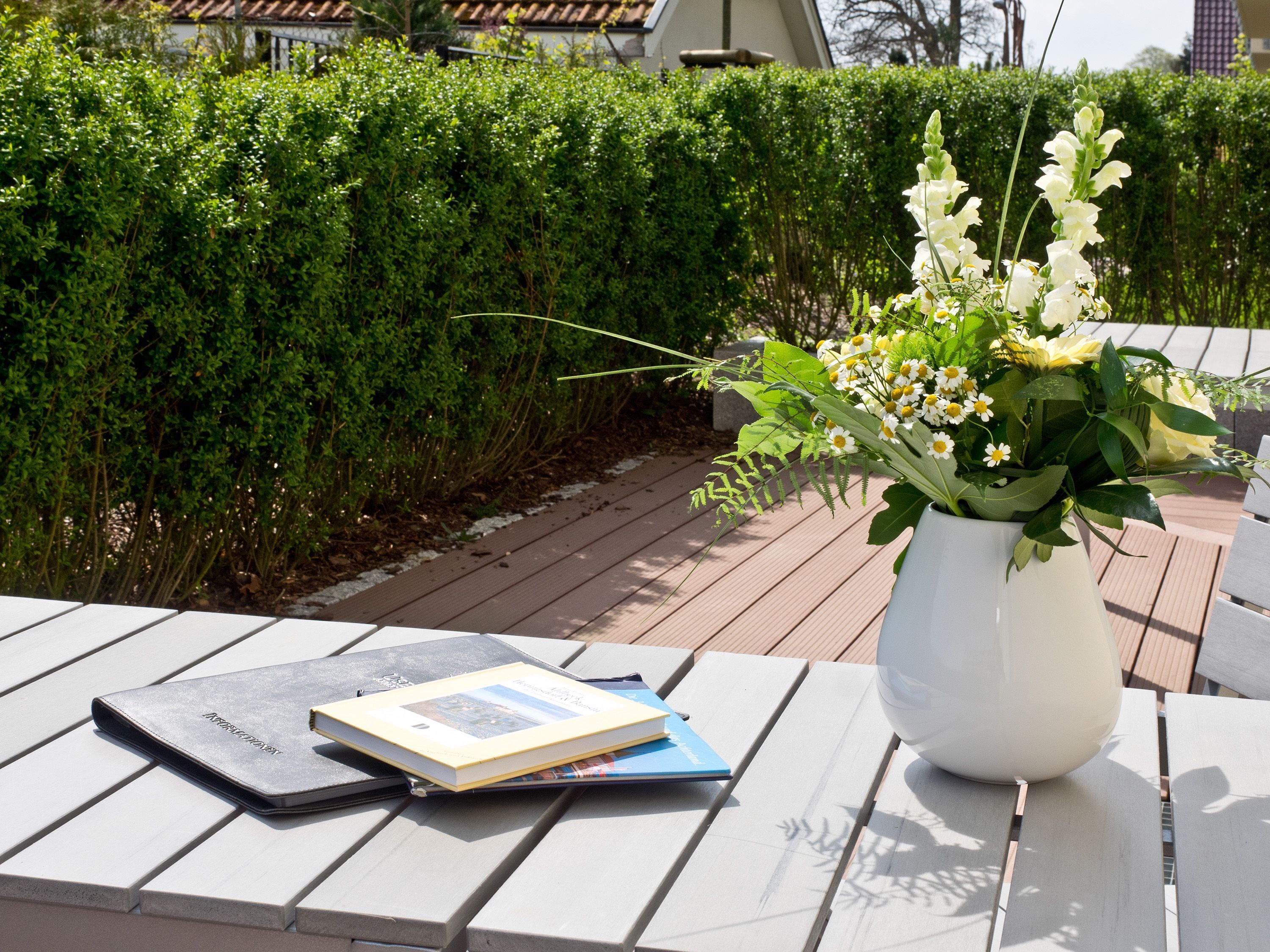 A white vase with flowers on a wooden table outdoors.