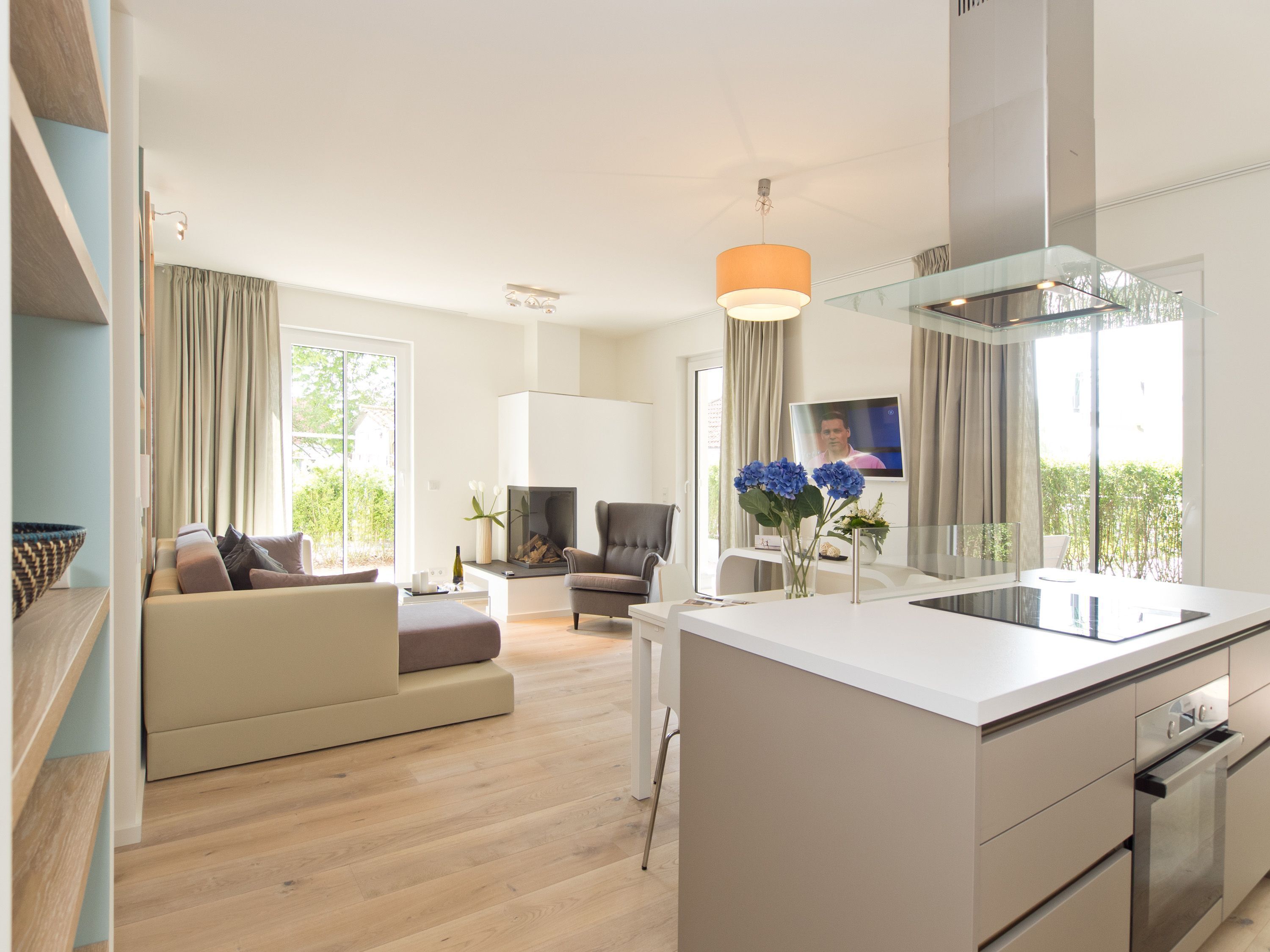 A modern kitchen with a central island, a dining area with a sofa and table, and a living room with a TV and a fireplace.