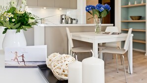 A modern kitchen with white cabinetry, a dining area with a white table and chairs, and a vase with blue flowers on the table. - Dünenpalais, App. 01 (Heringsdorf)